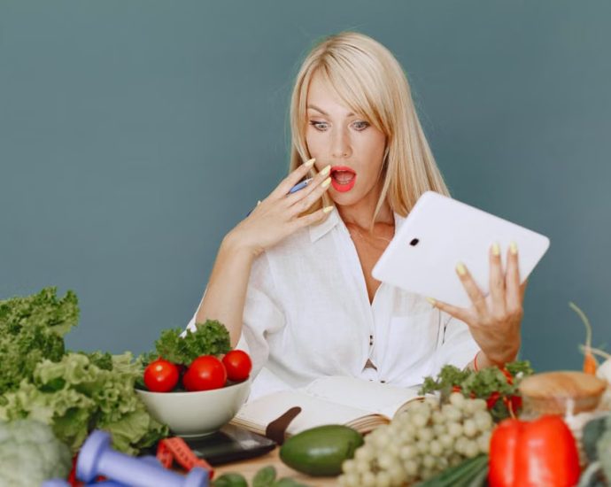 A surprised woman looking at a tablet surrounded by fresh vegetables and fruits, promoting healthy eating.