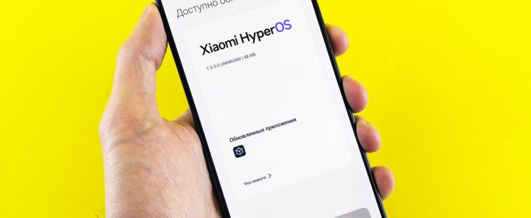 Hand holding smartphone showing Xiaomi HyperOS update screen on yellow background.