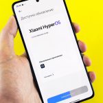 Hand holding smartphone showing Xiaomi HyperOS update screen on yellow background.